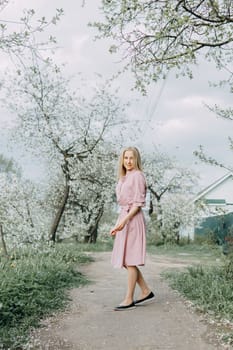 Blonde girl on a spring walk in the garden with cherry blossoms. Female portrait, close-up. A girl in a pink polka dot dress