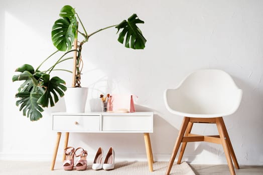 Stylish light room interior with elegant vanity table and monstera plants, beauty and fashion