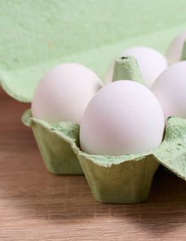 Fresh whole white eggs in green paper packaging on a wooden table