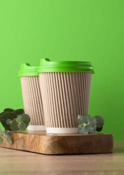 Paper brown cups with a plastic green lid for coffee and tea on a green background