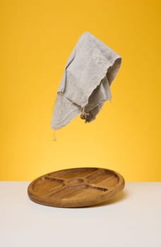 Round wooden board and gray napkin on yellow background