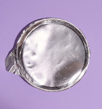 Aluminum round lid from under the package with chips on a purple background, flat lay