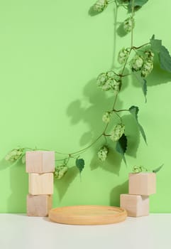 Round wooden empty podium and wooden cubes with branches and green leaves on a white table. Cosmetics advertising and display stage