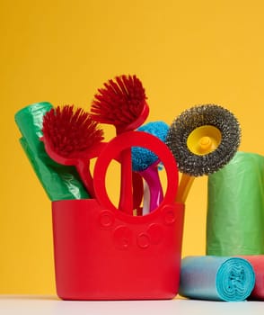 Plastic basket with brushes, disinfectant in a bottle on a yellow background. House cleaning items set