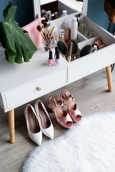 Stylish light room interior with elegant vanity table and plants, beauty and fashion. closeup of elegant high heel shoes standing under feminine dressing table