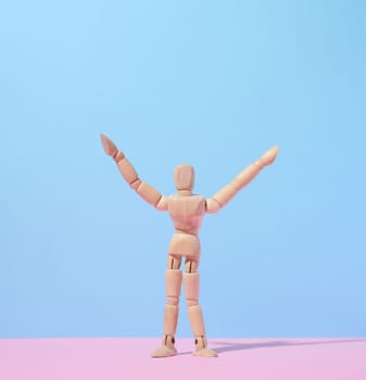 Wooden puppet man on a blue background, arms raised up