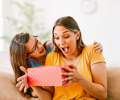 Daughter surprises her mother with present and kiss on mother's day or birthday at home