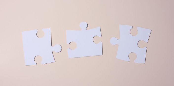 Empty white big puzzles on a beige background. Concept in business, flat lay