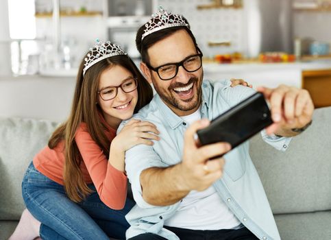 Family father and daughter having fun playing with princess crowns toys and making a selfie at home