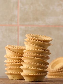 Stack of empty baked round canape baskets on a wooden board, round empty tartlets