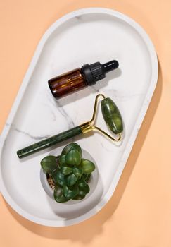 Hand held face massager and brown glass bottle with dropper on marble plate, top view