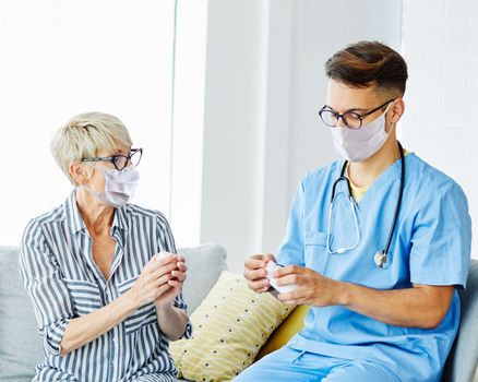 Doctor or nurse caregiver showing a prescrption drug bottle to senior woman wearing masks at home or nursing home