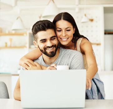 Portrait of a young happy smiling couple using laptop together at home. Wireless technology computer concept