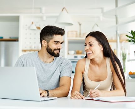 Portrait of a young happy smiling couple using laptop together at home. Wireless technology computer concept