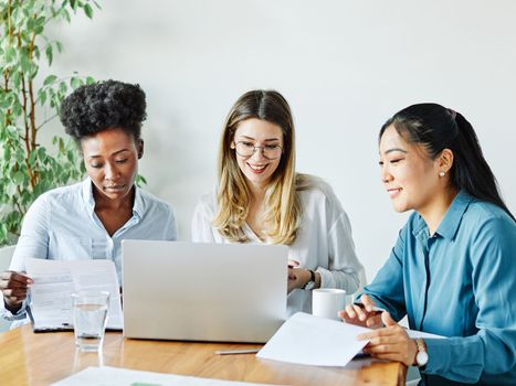 Portrait of a group of young businesswomen multiethnic working with laptop on desk and talking in a start up office