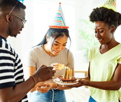 Group of young happy people friends having fun blowing candles on a birthday cake at home