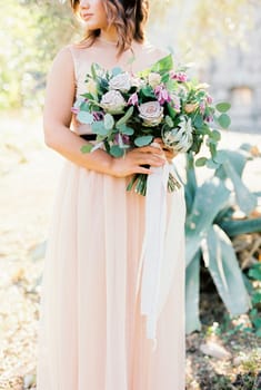Bouquet of flowers in the hands of the bride standing near the tree. High quality photo