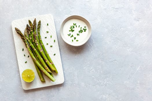 asparagus stems on the rectangular plate served with green lemon and parsley, grey concrete background, top view, copyspace