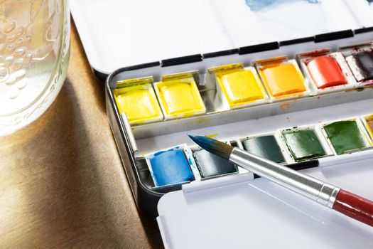 Watercolor tin with pans of colorful paint and brush with blue paint on tip