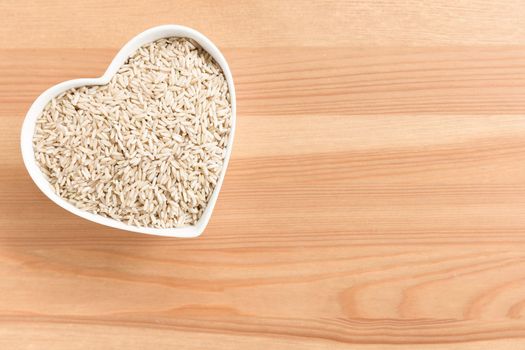 Flat lay of dried brown rice in a heart shaped bowl with copyspace.