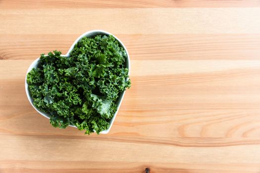 Flat lay of fresh raw kale in a heart shaped bowl with copy space