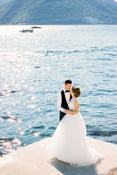 Groom hugs bride on the pier against the backdrop of mountains. High quality photo