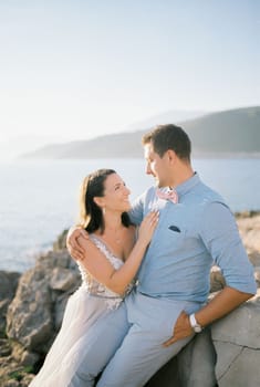 Bride and groom sit hugging on a rocky seashore. High quality photo