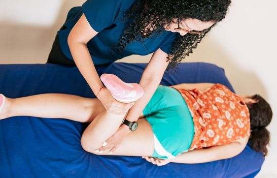 Top view of Chiropractor stretching knee to lying female patient, Knee flexion physiotherapy to female patient. Physiotherapist woman assisting knee to lying patient