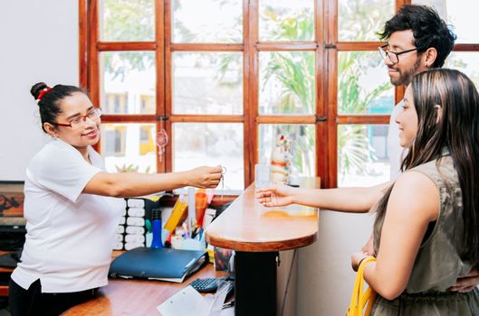 Latin couple receiving hotel room keys. Woman receptionist giving hotel room key to couple, Concept of couple arriving at hotel, Receptionist giving hotel room keys to couple