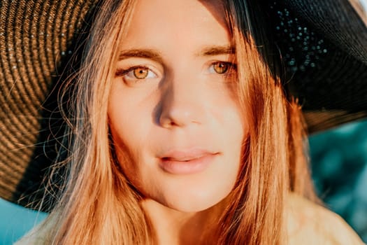 Portrait of happy young woman wearing summer black hat with large brim at beach on sunset. Closeup face of attractive girl with black straw hat. Happy young woman smiling and looking at camera at sea