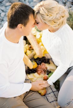 Man and woman holding hands, touching foreheads, sitting on a blanket. High quality photo