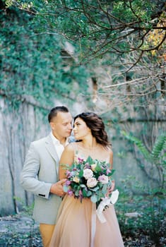 Groom hugs from behind bride with a bouquet, who turned her head to him. High quality photo