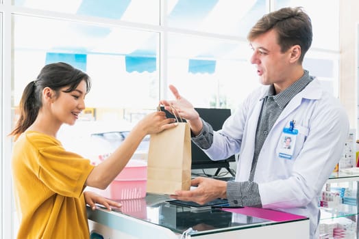 Affable pharmacist give or handing customer a bag of qualified medications or medical supplies, customer service concept in pharmacy. Pharmacist working on cashier talking to customer in drugstore.