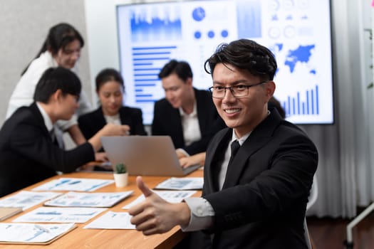 Focus portrait of successful confident male manager or executive in business wear with blurred background of businesspeople, colleagues working with financial report papers in office of harmony.
