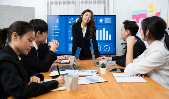 Confidence and young asian businesswoman give presentation on financial business strategy in dashboard report display on screen to colleagues in conference room meeting as harmony in workplace concept