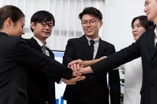 Closeup business team of suit-clad businessmen and women join hand stack together and form circle. Colleague collaborate and work together to promote harmony and teamwork concept in office workplace.