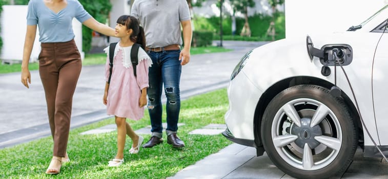 Progressive young happy family with electric vehicle and home backyard charging station. Green and clean energy from electric vehicles for healthy environment. Eco power from renewable source.