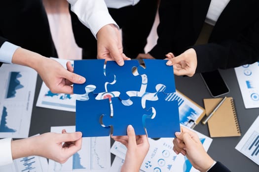 Closeup top view business team of office worker putting jigsaw puzzle together over table filled with financial report paper in workplace with manager to promote harmony concept in meeting room.