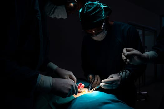 Surgical team performing surgery to patient in sterile operating room. In a surgery room lit by a lamp, a professional and confident surgical team provides medical care to an unconscious patient.