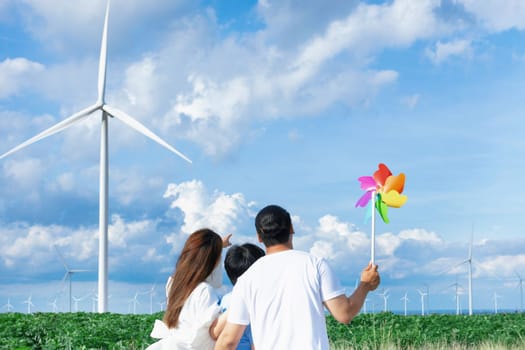 Concept of progressive happy family enjoying their time at the wind turbine farm. Electric generator from wind by wind turbine generator on the country side with hill and mountain on the horizon.