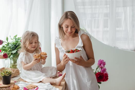 A little blonde girl with her mom on a kitchen countertop decorated with peonies. The concept of the relationship between mother and daughter. Spring atmosphere.