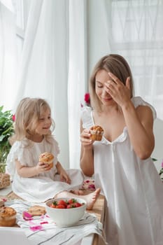 A little blonde girl with her mom on a kitchen countertop decorated with peonies. The concept of the relationship between mother and daughter. Spring atmosphere.