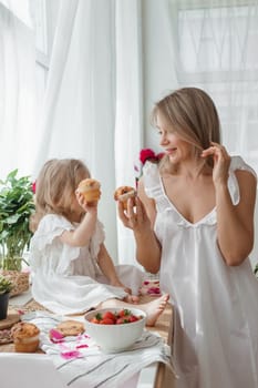 A little blonde girl with her mom on a kitchen countertop decorated with peonies. The concept of the relationship between mother and daughter. Spring atmosphere.