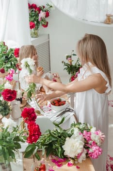 A little blonde girl with her mom on a kitchen countertop decorated with peonies. The concept of the relationship between mother and daughter. Spring atmosphere.