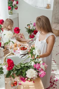 A little blonde girl with her mom on a kitchen countertop decorated with peonies. The concept of the relationship between mother and daughter. Spring atmosphere.