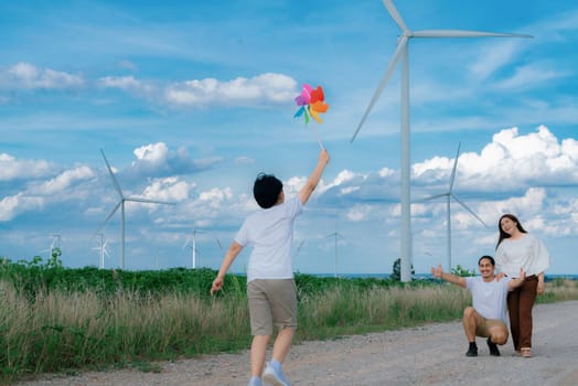 Progressive happy family enjoying their time at wind farm for green energy production concept. Wind turbine generators provide clean renewable energy for eco-friendly purposes.
