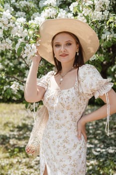 An attractive long-haired woman walks in the spring in the park of blooming apple trees. Spring portrait of a woman