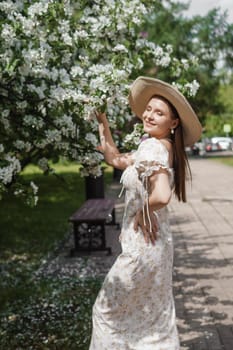 An attractive long-haired woman walks in the spring in the park of blooming apple trees. Spring portrait of a woman