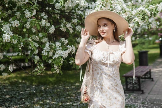 An attractive long-haired woman walks in the spring in the park of blooming apple trees. Spring portrait of a woman