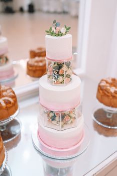 White wedding cake decorated by flowers standing on festive table with lots of snacks on side. Violet flowers on foreground. Wedding. Recetion. High quality photo